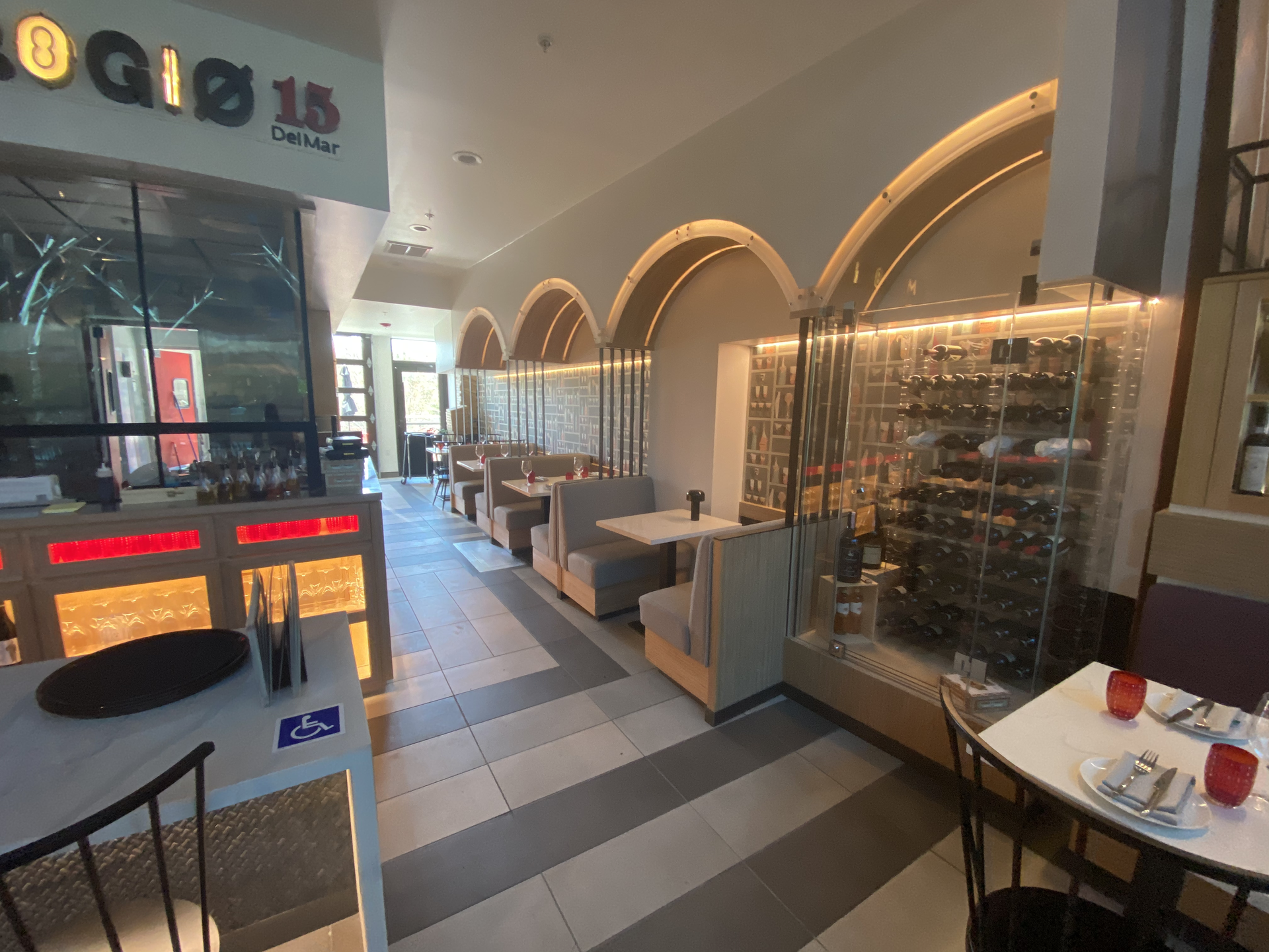 Indoor shopping mall seating area with arched storefronts and a glass wine display on the right.