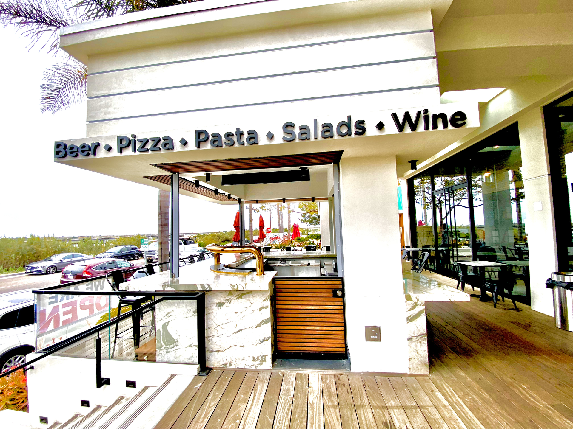 Outdoor restaurant patio with a sign reading “Beer • Pizza • Pasta • Salads • Wine”