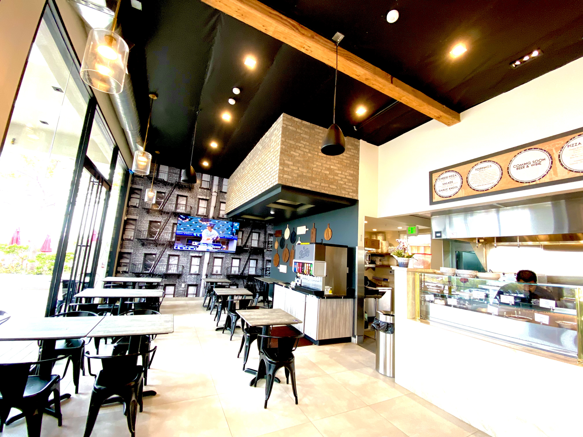 Modern café interior with tables, black chairs, pendant lights, and a counter service area.