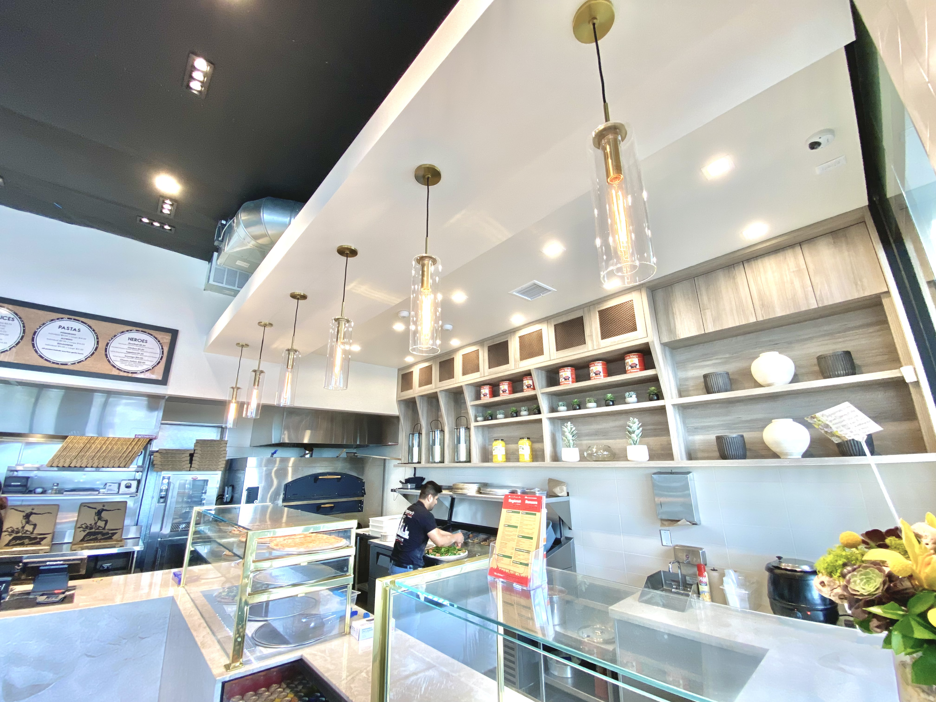 Bright café counter with glass pastry cases, white shelves, hanging pendant lights, and jars on display