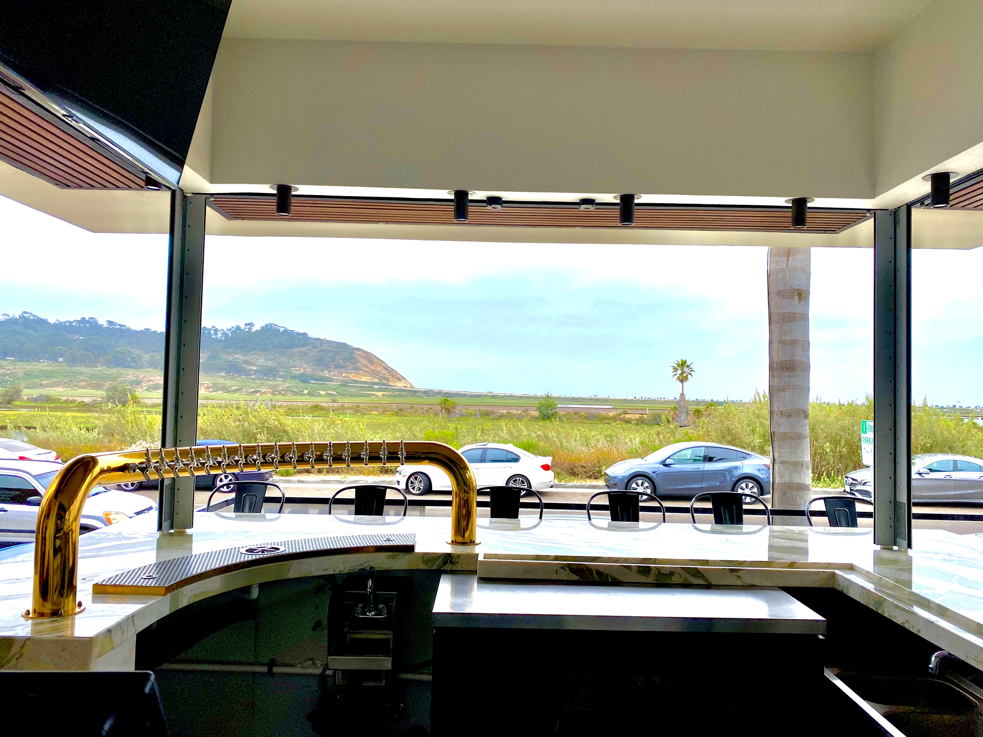 Covered outdoor seating area with railings overlooking a road, cars, and green hills under a cloudy sky
