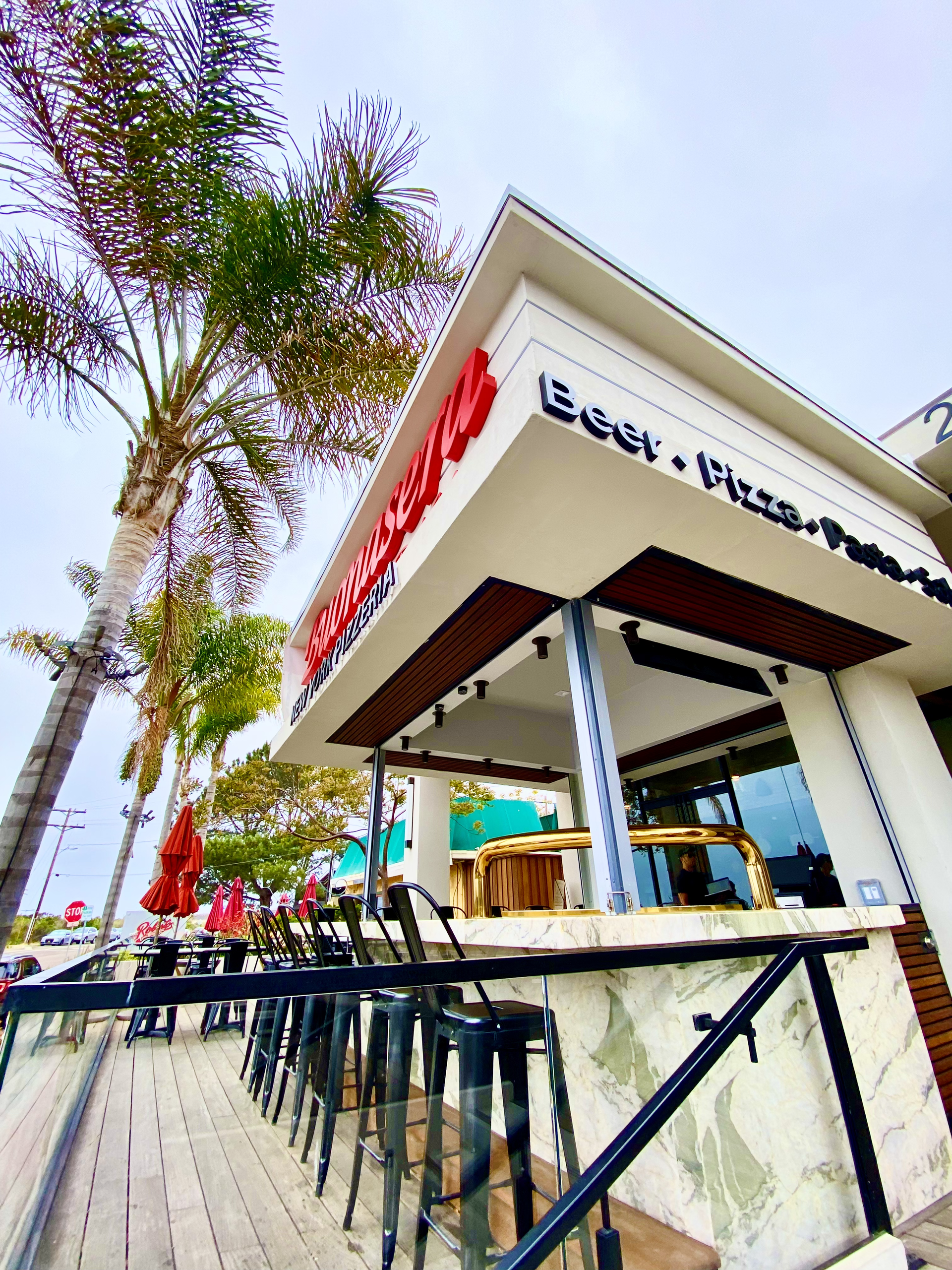 Outdoor view of a modern beachfront cafe with palm trees and red signage