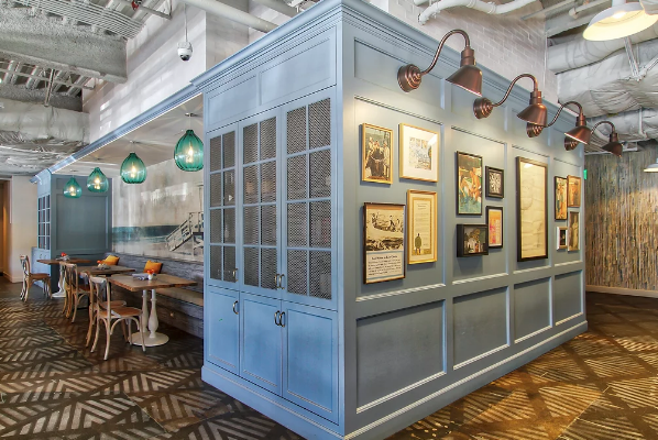 Restaurant booth with blue paneled walls and framed art, beside a dining area with hanging lights
