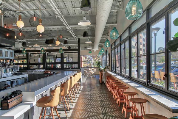 Bright cafe interior with long bar seating, large windows, and hanging lights on a sunny day