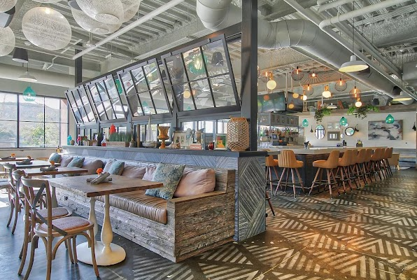 Bright modern café interior with long tables, leather seating, hanging lights, and patterned floor tiles