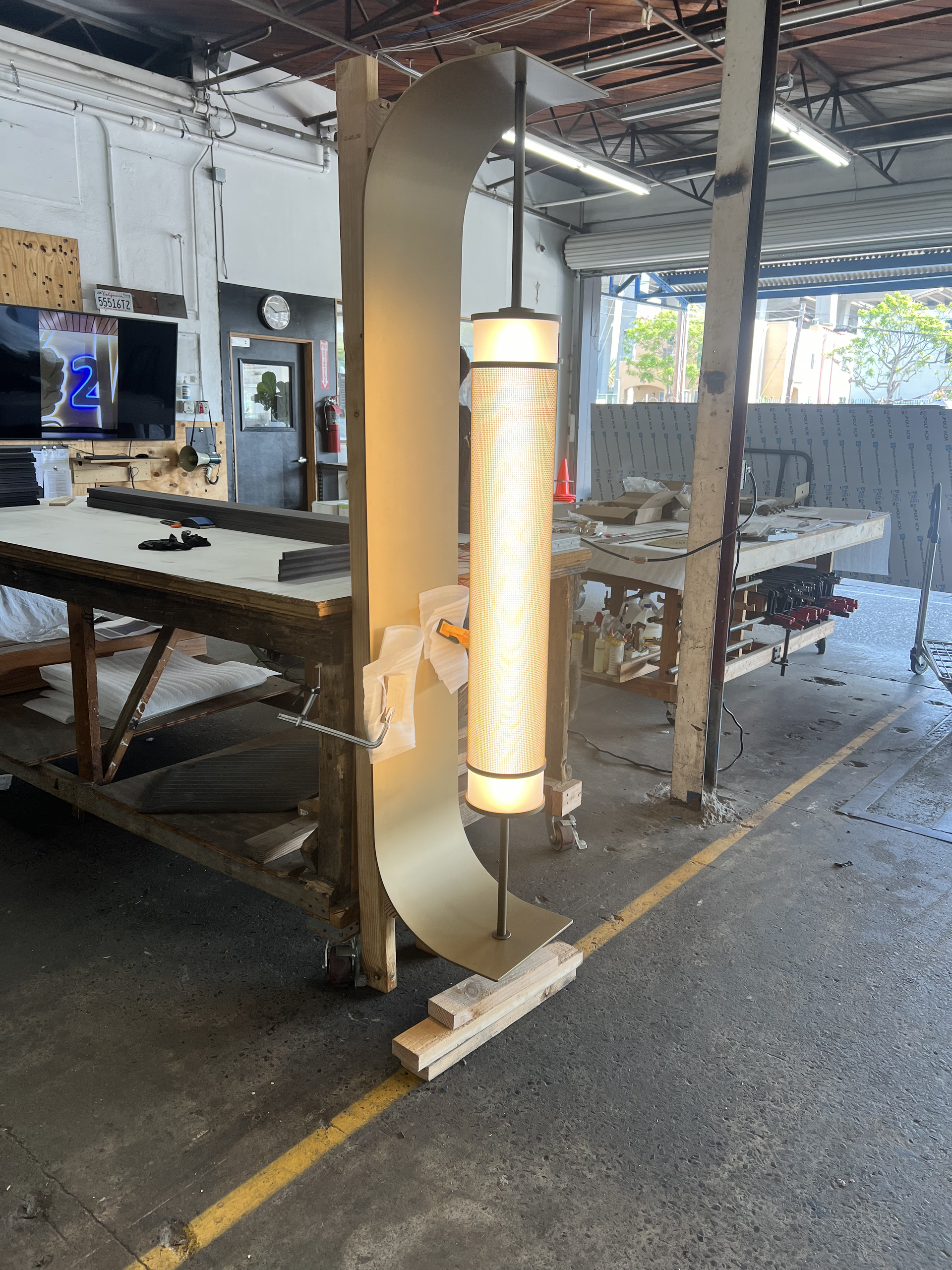 Tall cylindrical floor lamp glowing in a workshop aisle beside workbenches and a table saw.