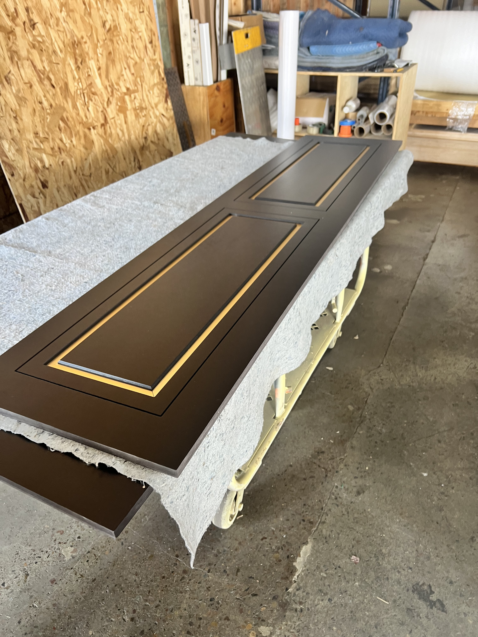 Long dark-brown wooden table on a foam-wrapped pallet in a workshop.