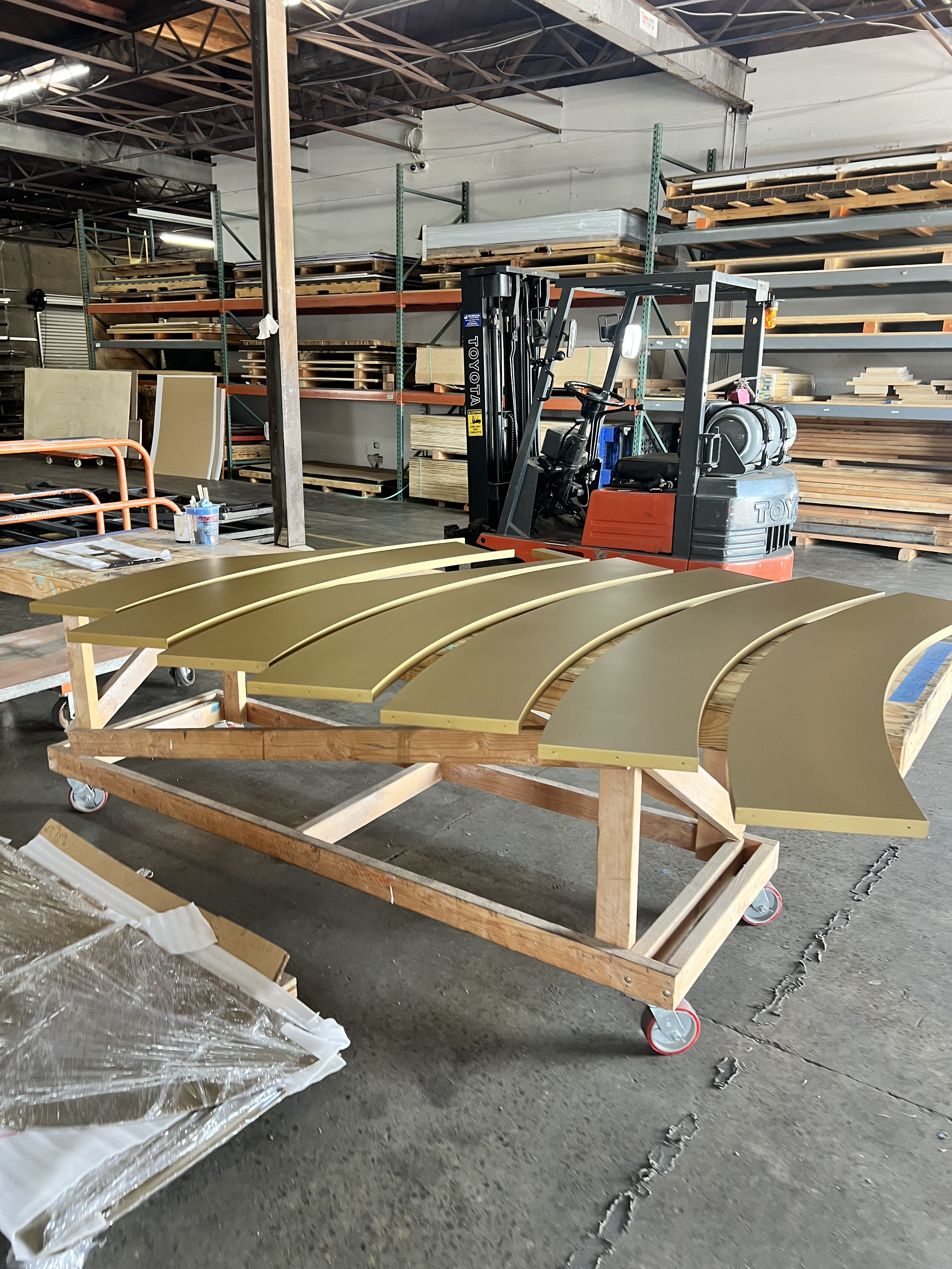 Curved metal panels on a wooden cart in a workshop with a forklift in the background