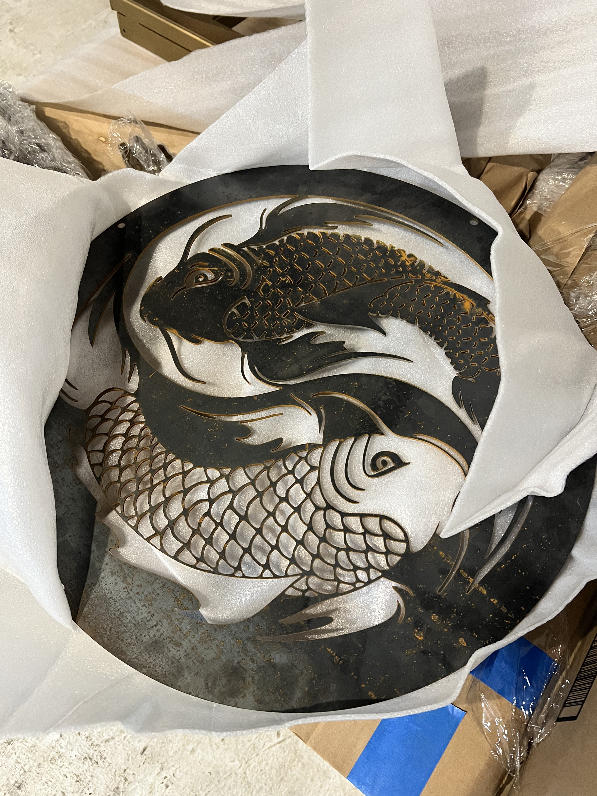 Black-and-white fish illustration on a round plate, wrapped in white paper inside a cardboard box