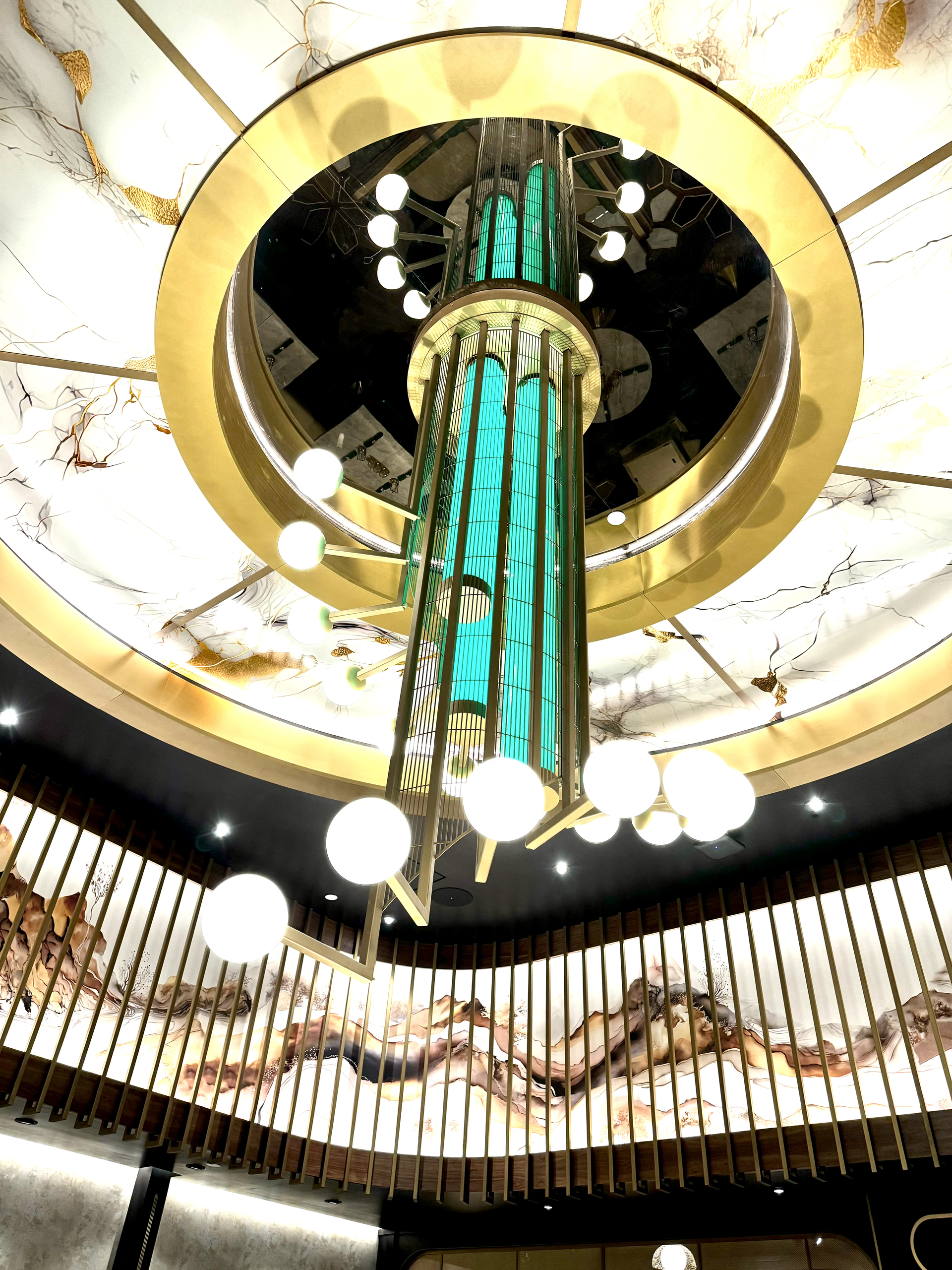Grand chandelier hanging from a circular ceiling with gold accents and green glass panels