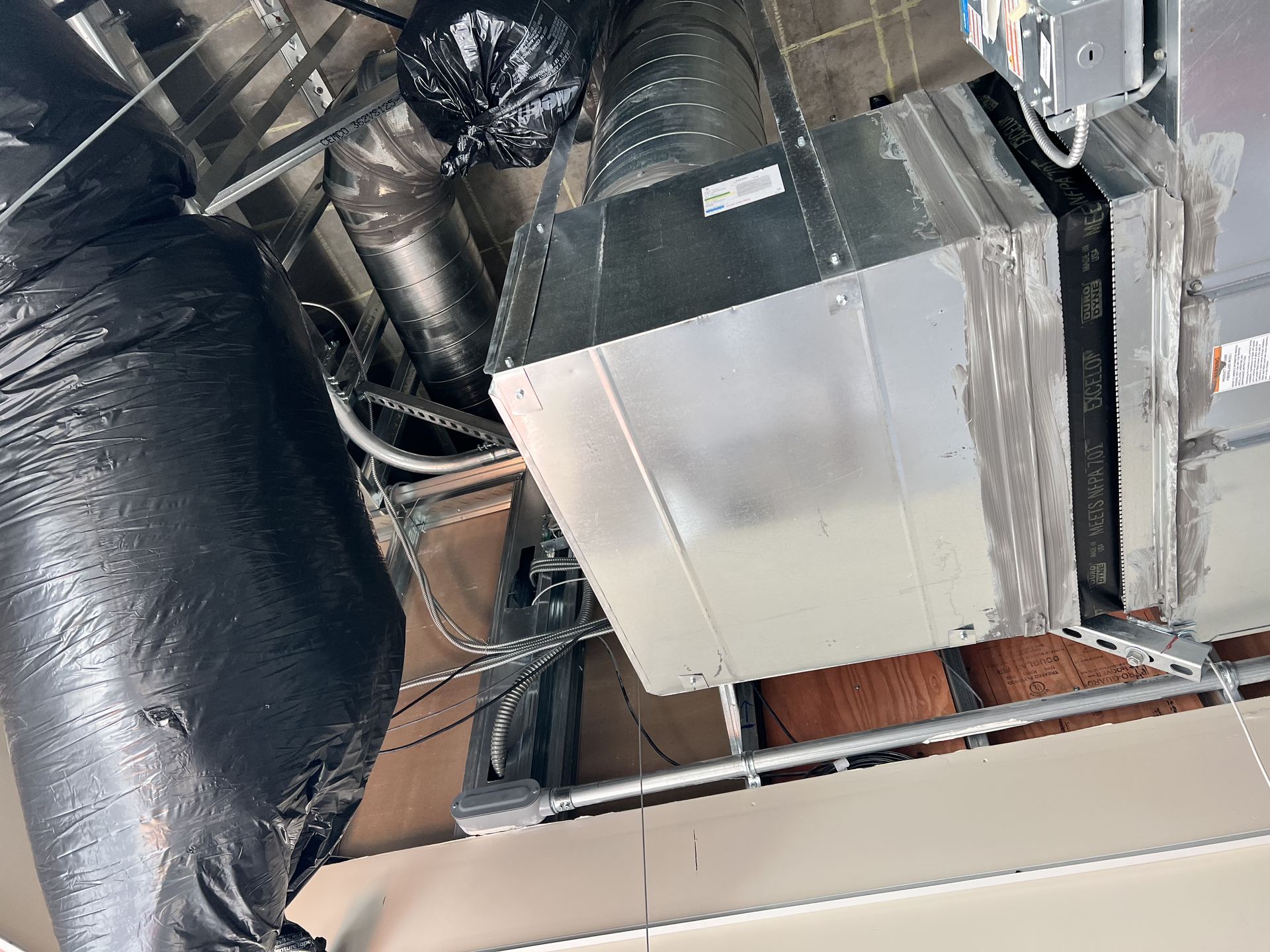 Ceiling ductwork and a large metal HVAC unit in an unfinished attic space