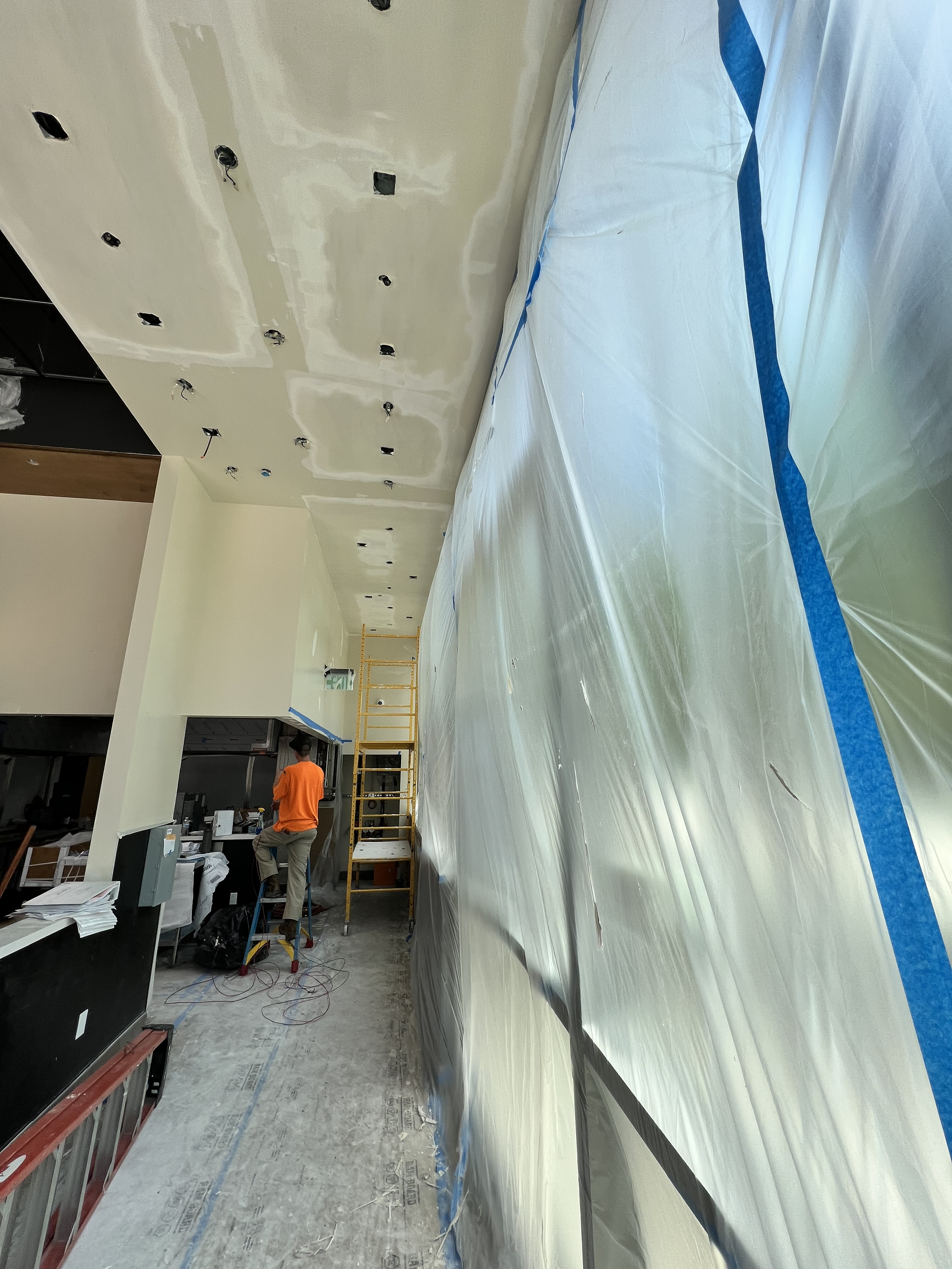 Construction corridor with covered wall, worker in orange vest, and equipment on a dusty floor