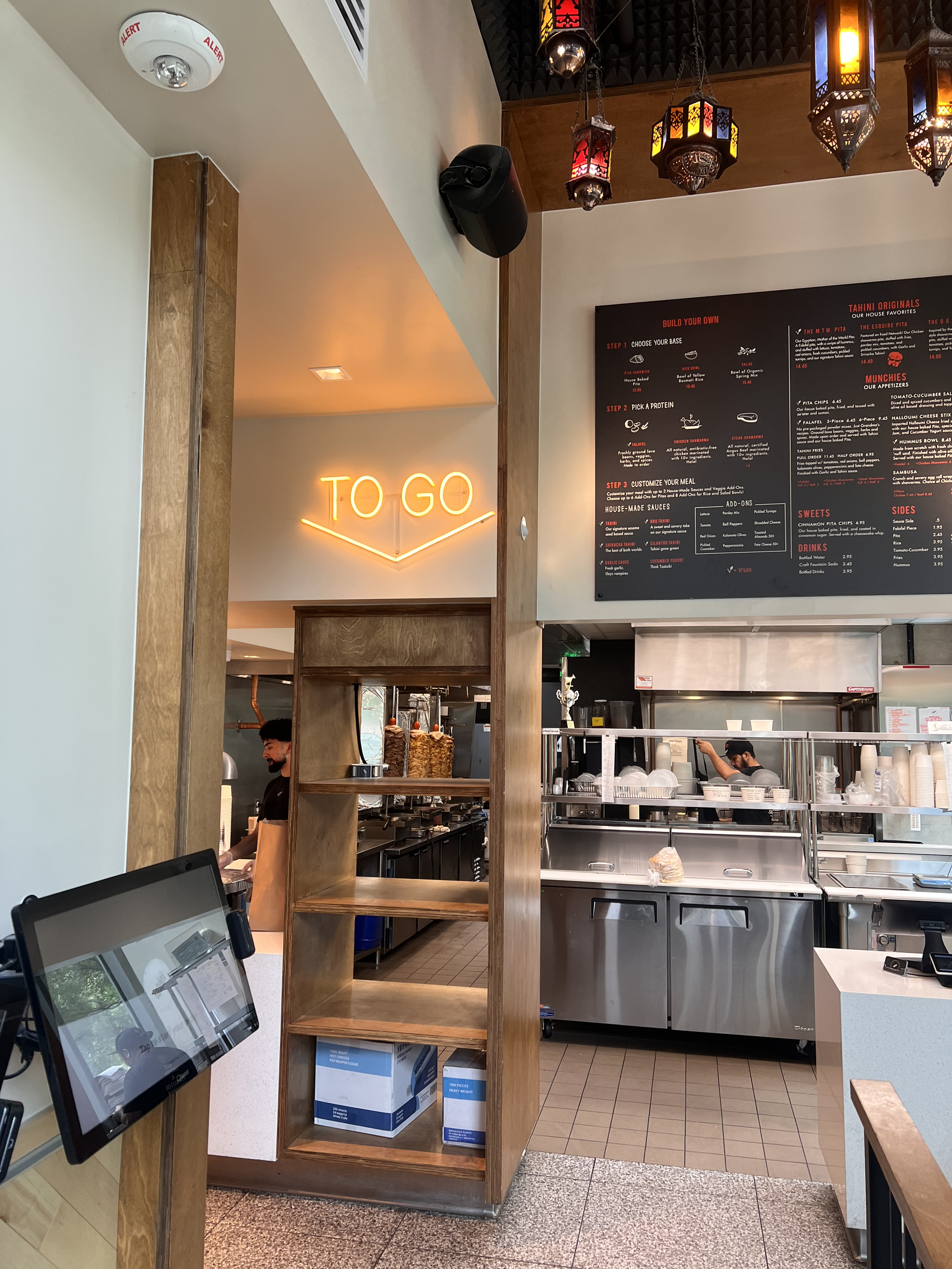 Modern café interior with neon “TO GO” sign, menu board, and staff behind the counter