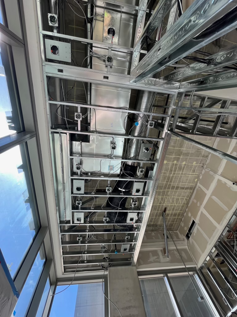 Ceiling with exposed metal framework and ducts in an industrial-looking interior, with blue sky visible through skylights
