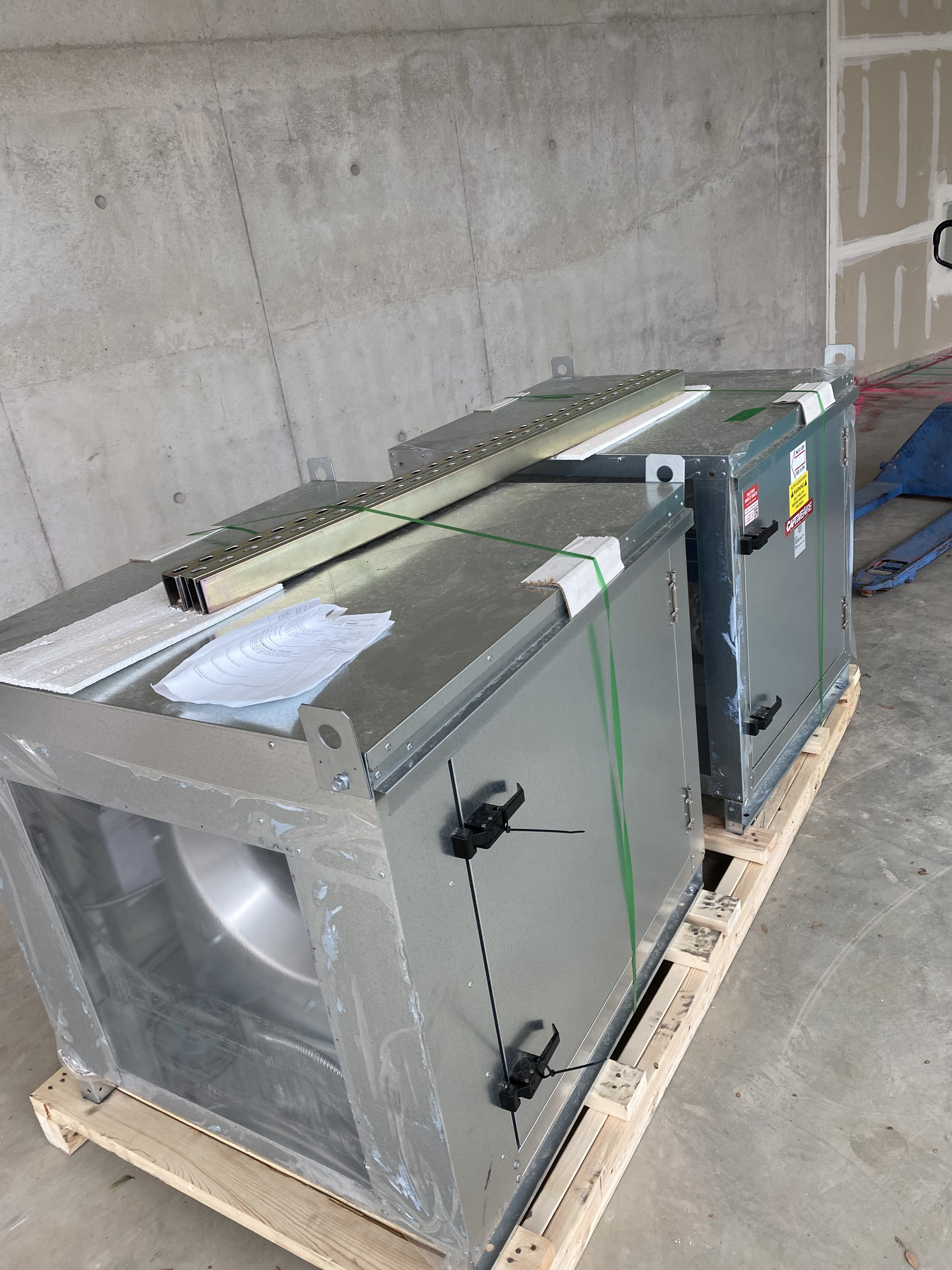 Two gray HVAC units strapped on a wooden pallet in a warehouse setting