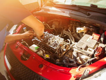 A man is working on the engine of a red car.
