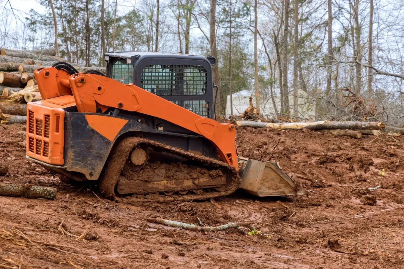 Orange skid steer pushing dirt on a muddy construction site with trees in the background