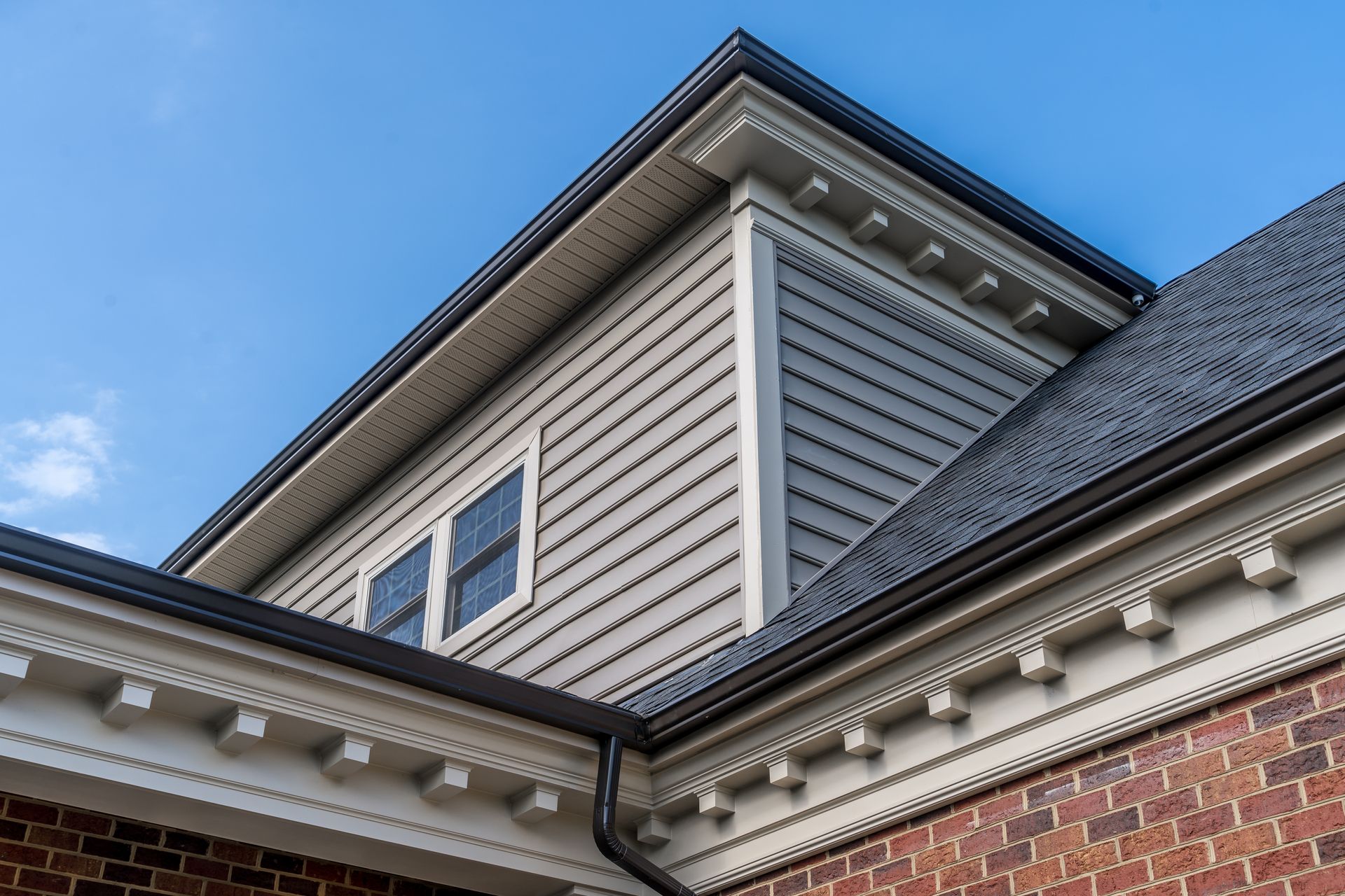 Corner of a building with gray siding, brick, and decorative white trim against a blue sky.