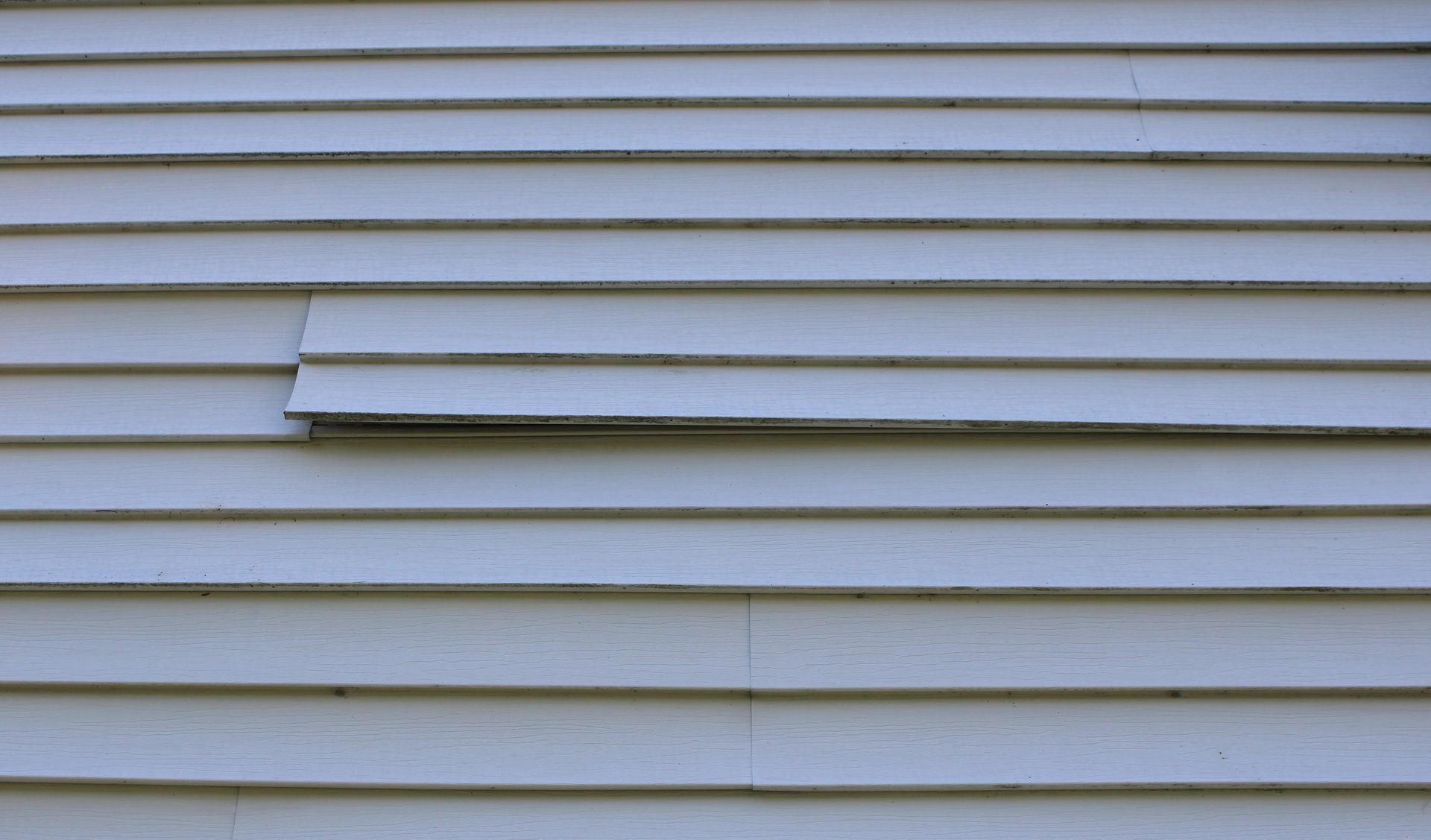 White clapboard siding with a damaged plank protruding outward.