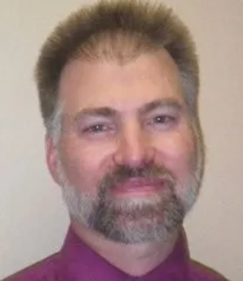 A man with a beard and a purple shirt is smiling for the camera.