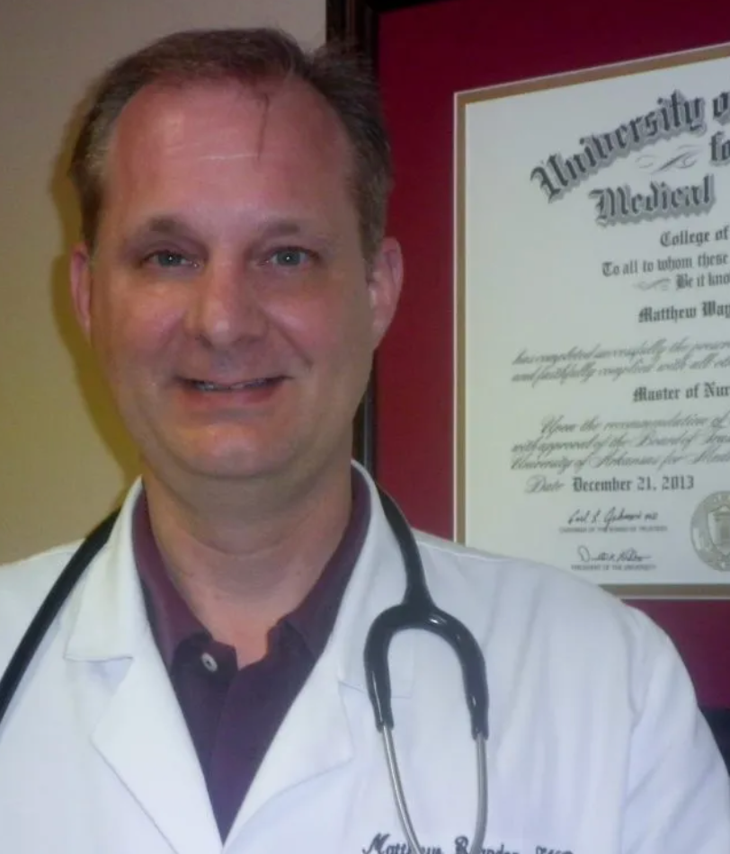 A man with a stethoscope around his neck stands in front of a university of medicine certificate