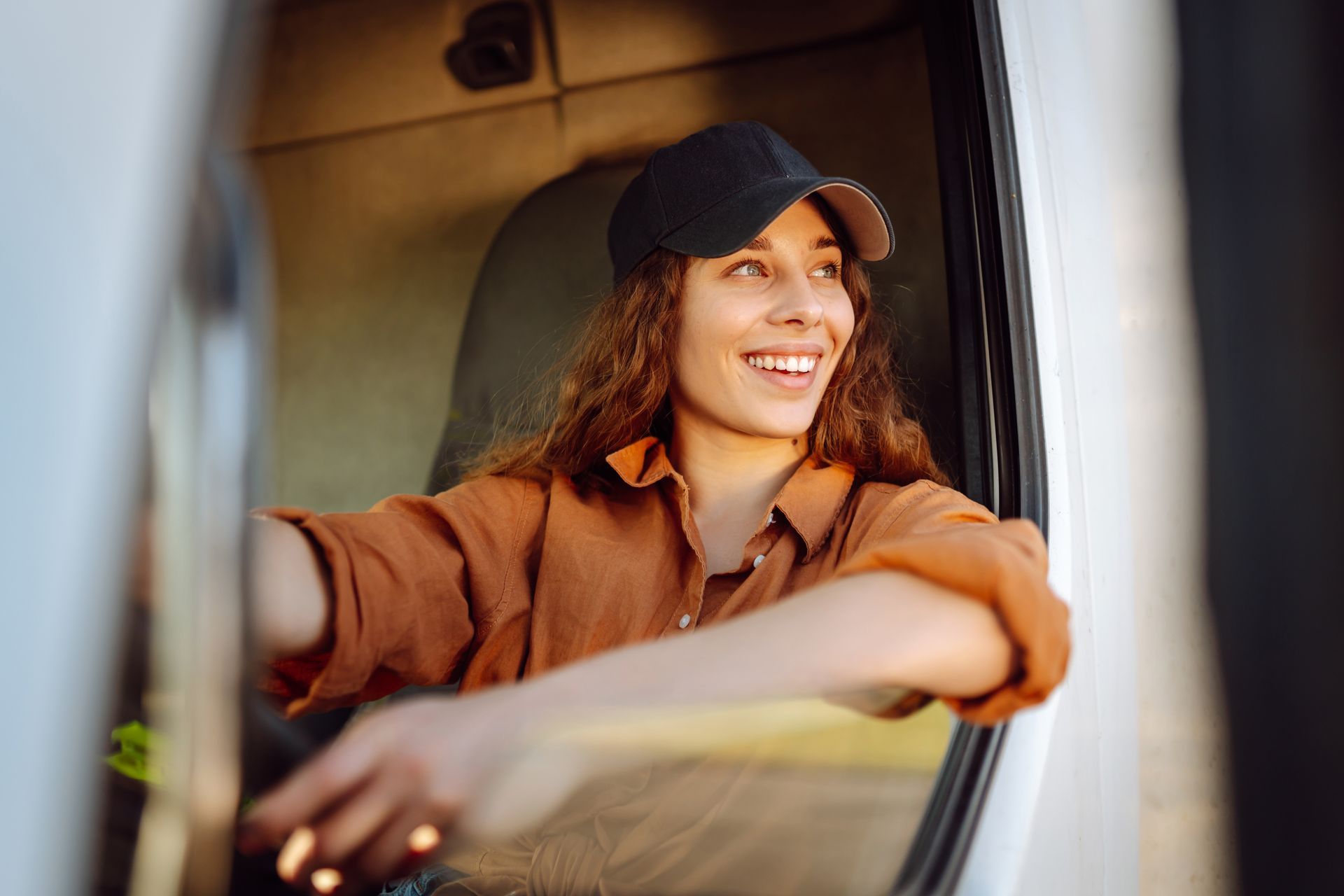 A woman is sitting in the driver 's seat of a truck looking out the window.