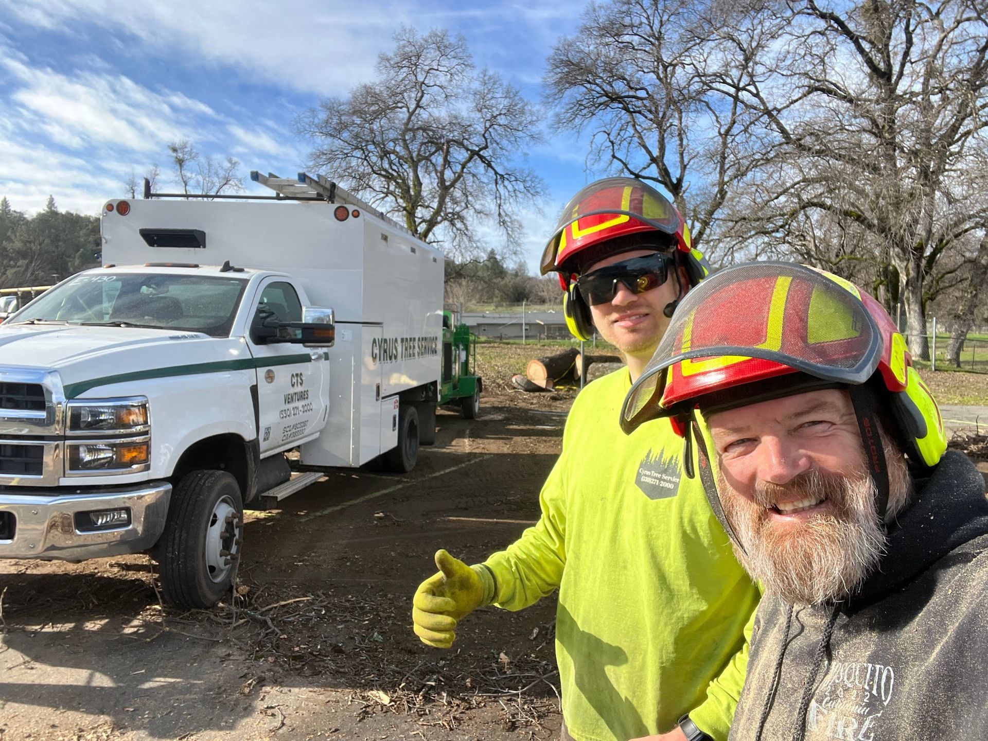 Two workers in safety gear posing beside a white utility truck at a muddy work site.