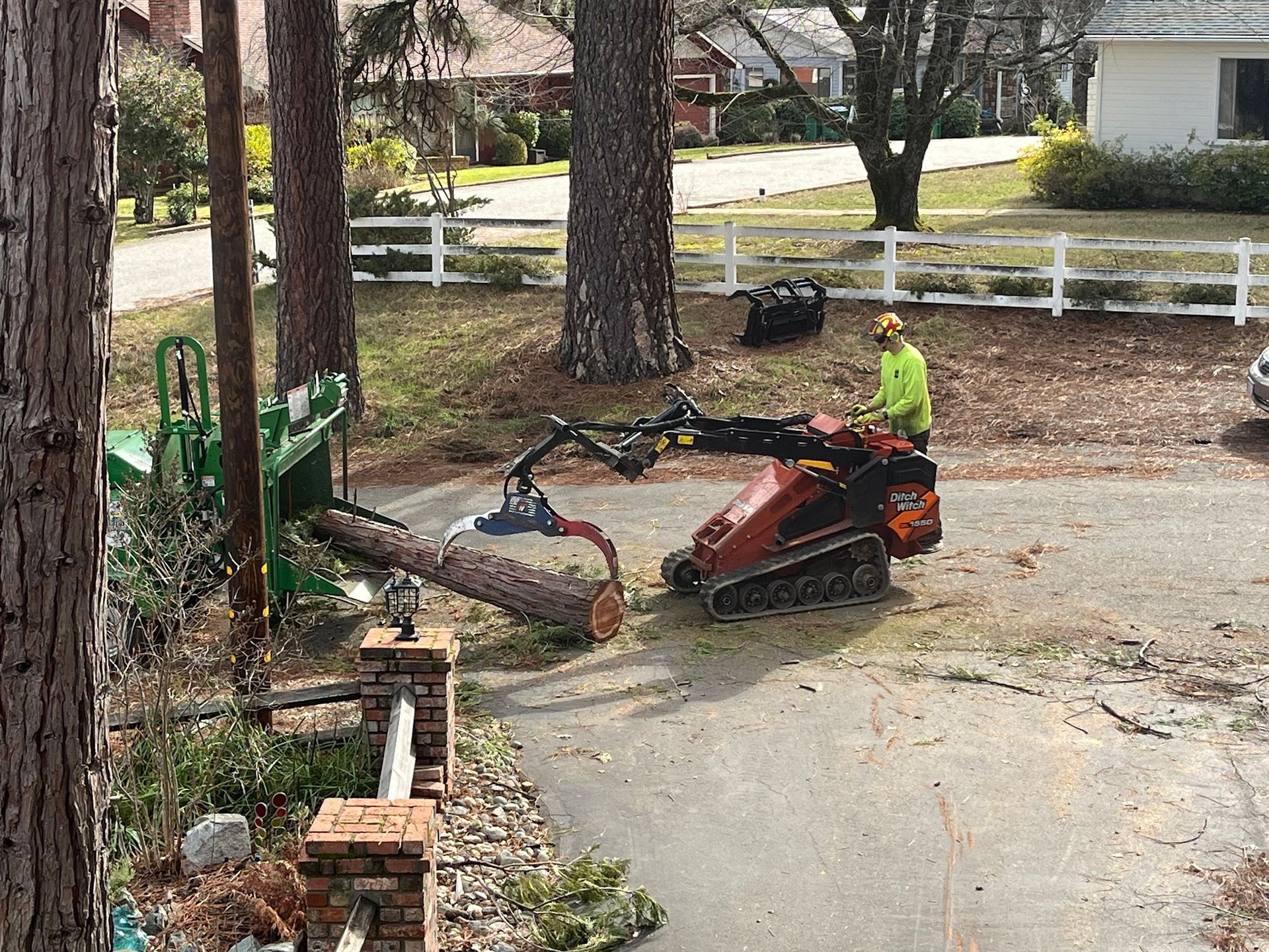 Worker operating a red excavator clearing debris beside a house on a muddy driveway