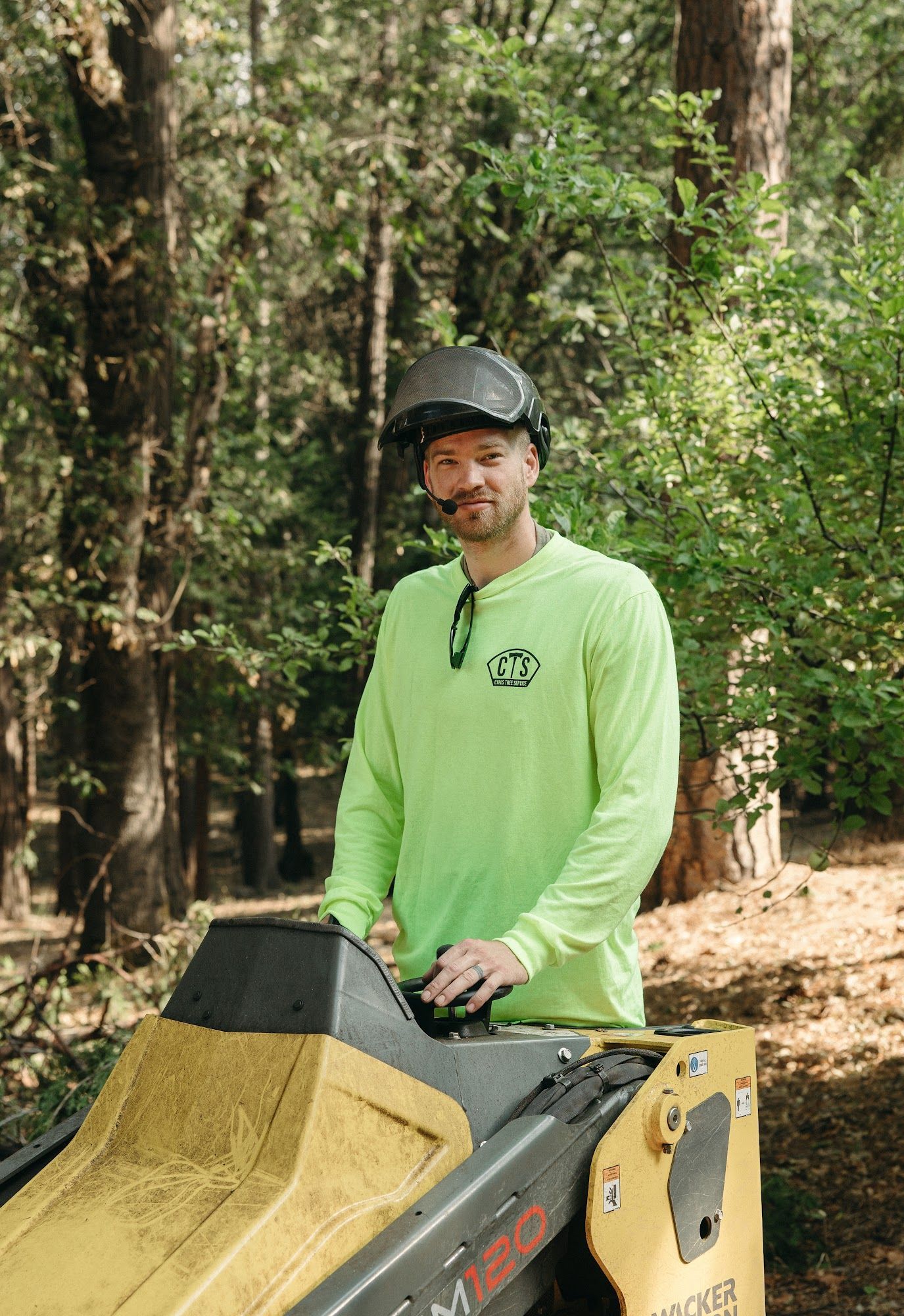 Person in a neon green shirt standing beside a yellow off-road vehicle in a wooded area