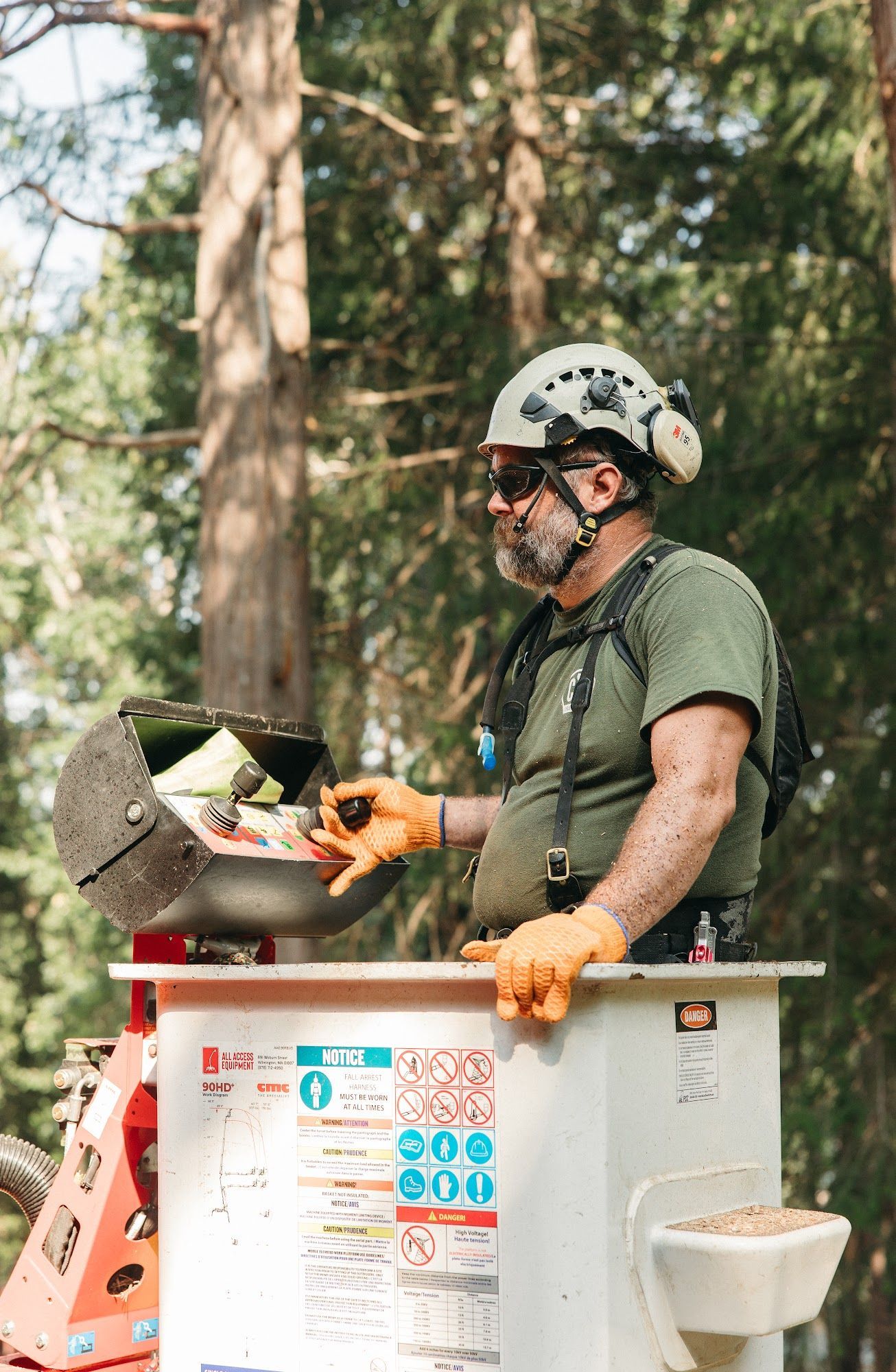 Worker in helmet and gloves using a chainsaw in a bucket lift among trees