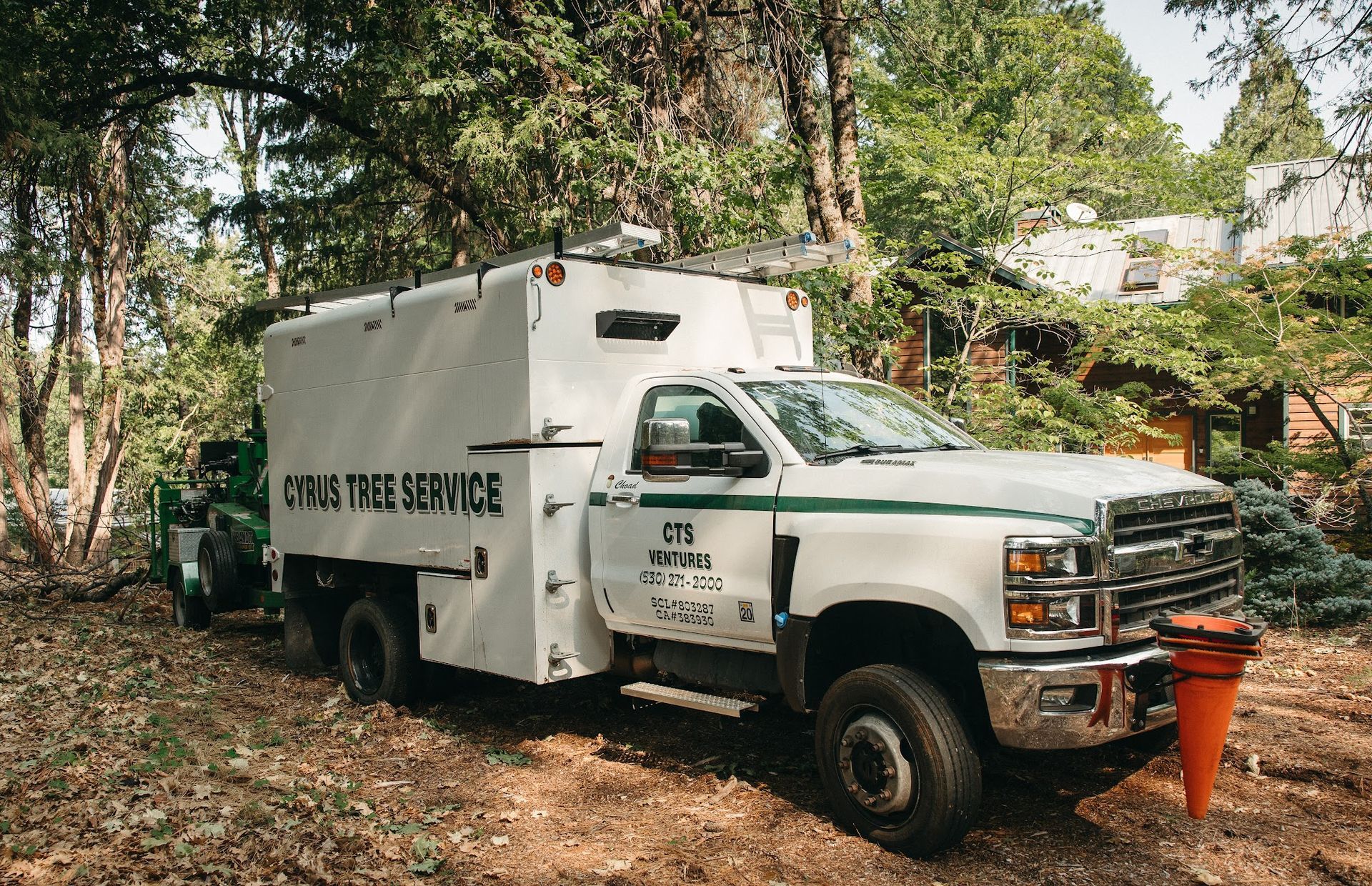 White utility truck with “Beyond the Service” parked on a wooded dirt path, carrying an orange cone.