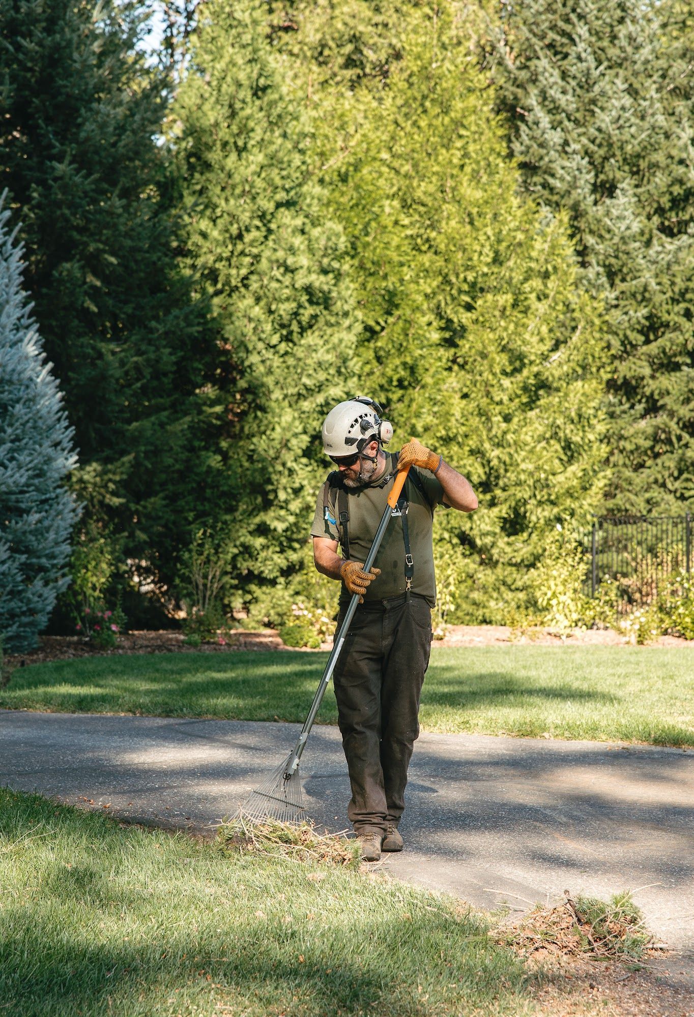 Person using a string trimmer along a paved path in a wooded park.
