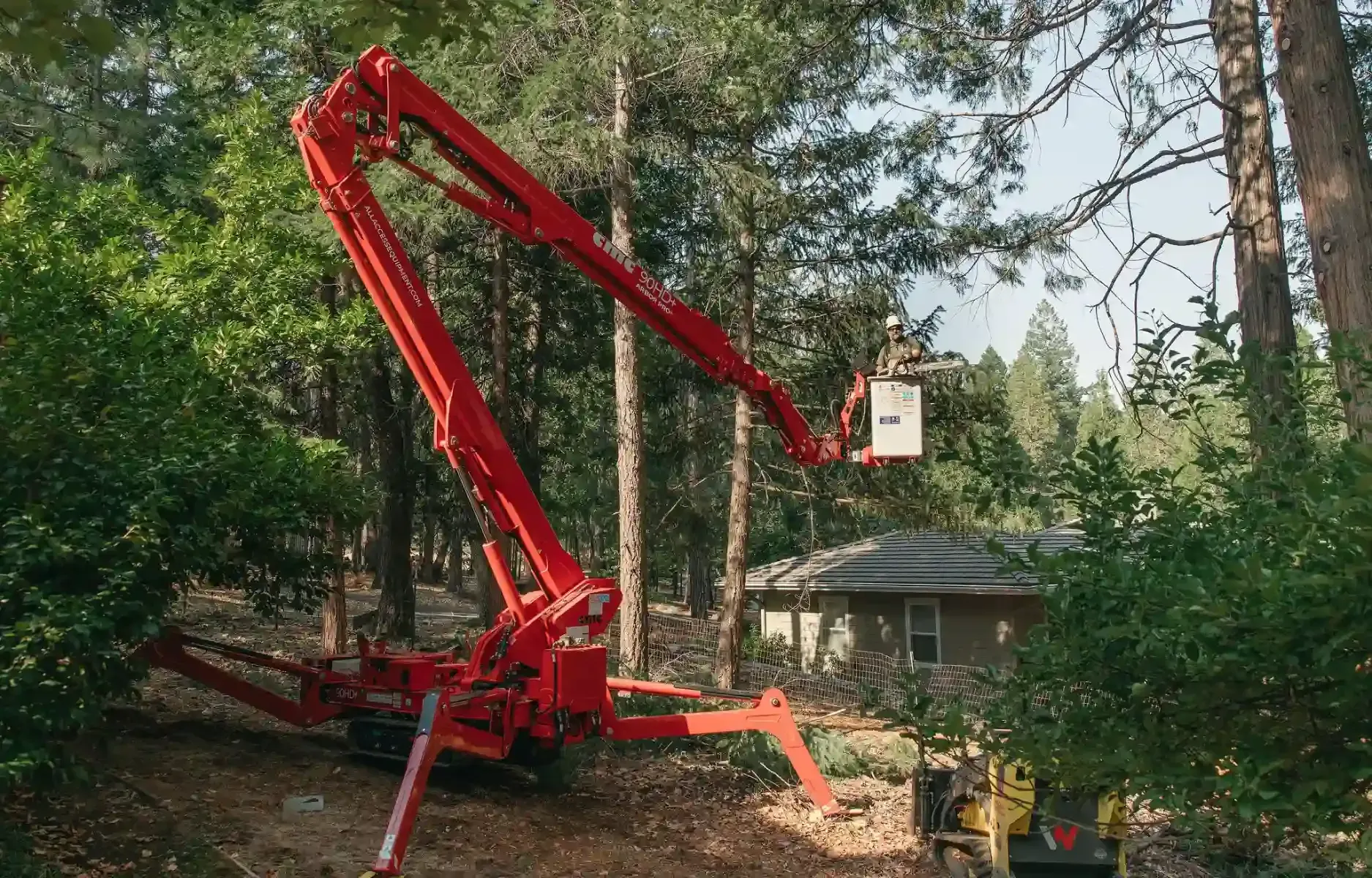 Red crane lift arm beside a house in a wooded yard