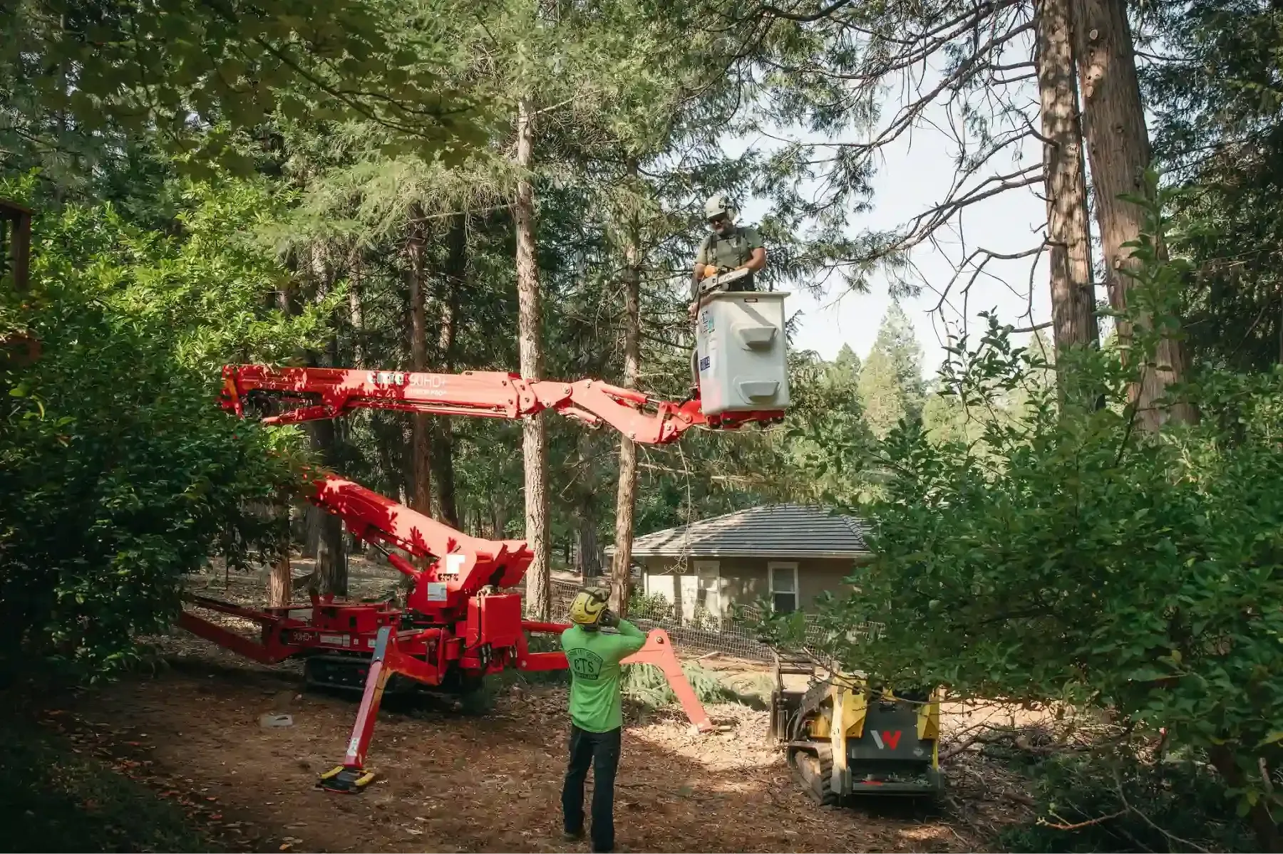 Worker using red crane to lift a white hot tub in a wooded yard near a house