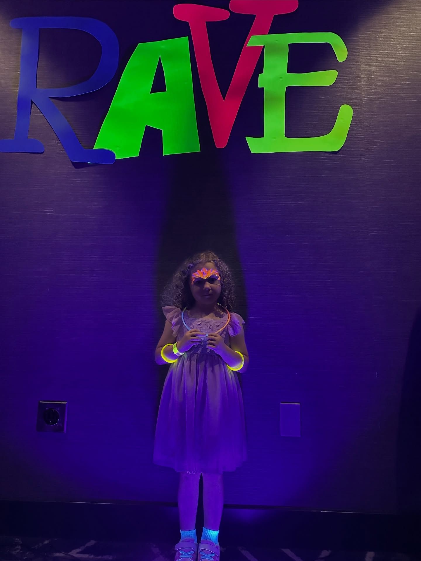 Girl in a dress and glow bracelets stands in front of a 