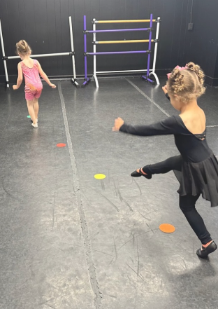 Two young dancers in a studio, practicing kicks over colored spots.