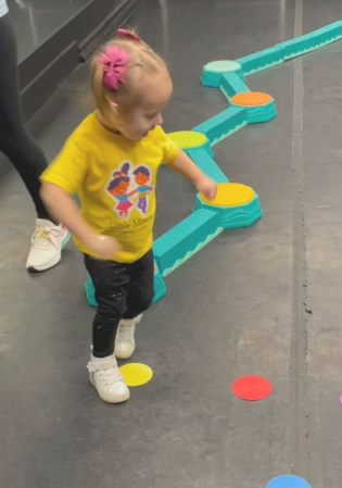 Girl in yellow shirt with pink bow, playing on a colorful stepping stone path.