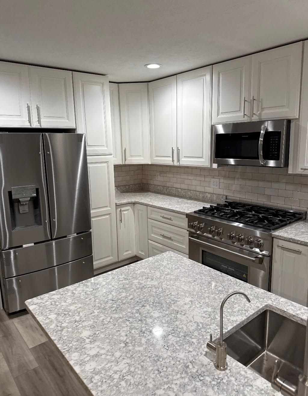 Modern white kitchen with stainless steel appliances, granite island, and recessed lighting