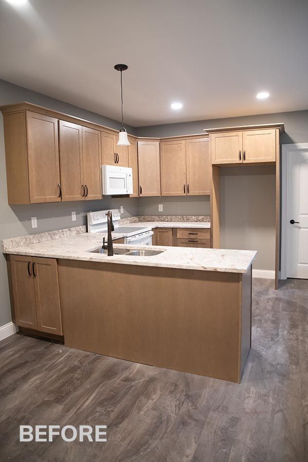Before photo of an empty kitchen with light wood cabinets, granite island, and gray flooring