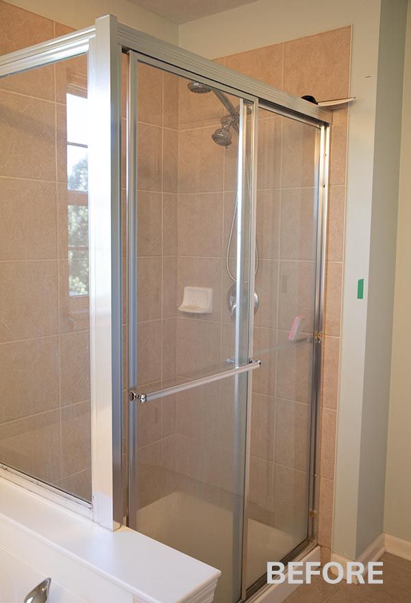 Glass shower enclosure in a beige-tiled bathroom, with a bathtub visible on the left.