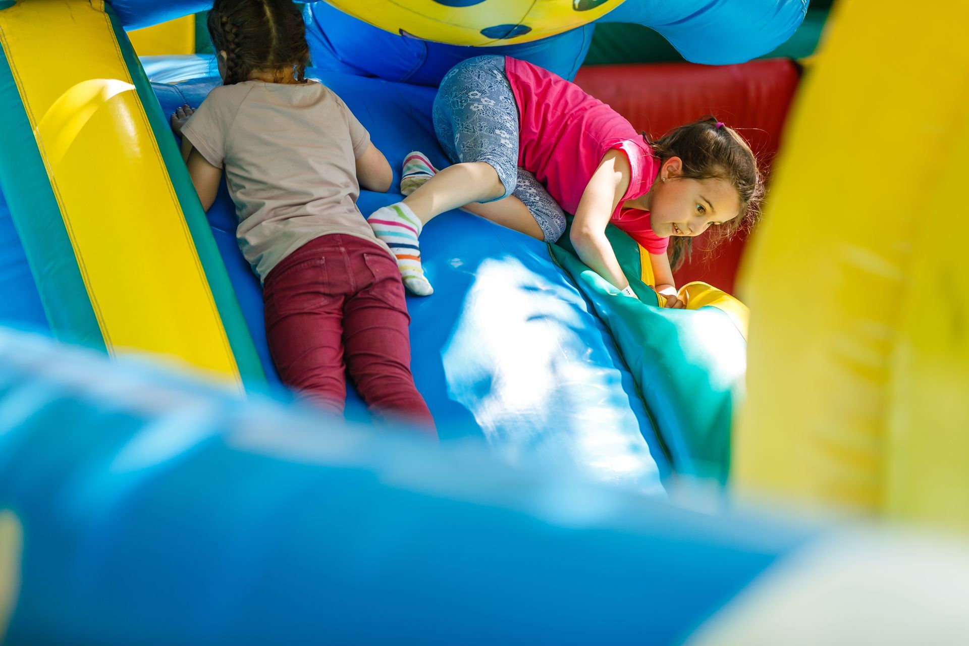 Two children climbing inside a colorful inflatable bounce house.