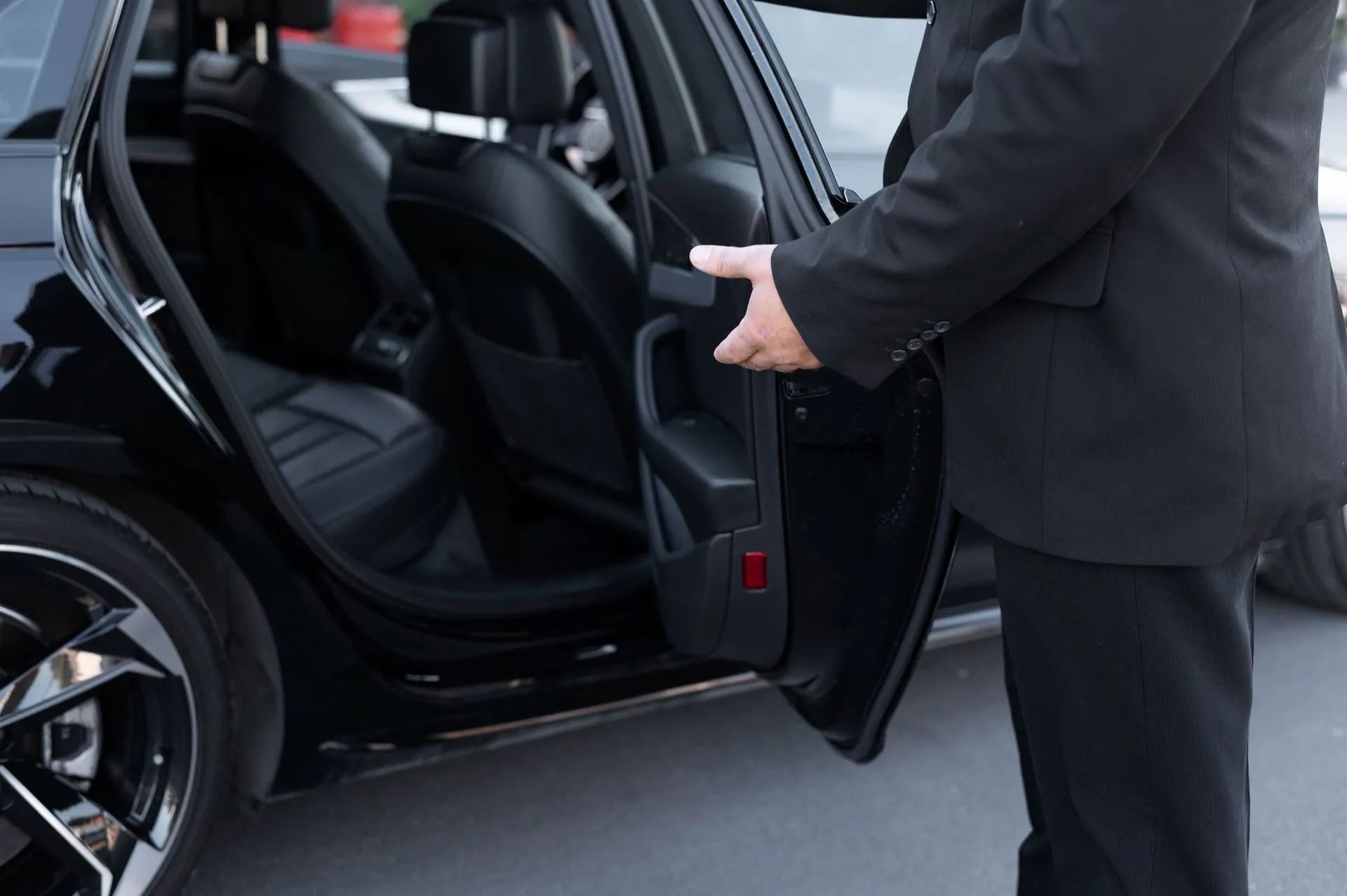 Una persona sostiene abierta la puerta de un coche negro junto a otro vehículo negro en la calle.