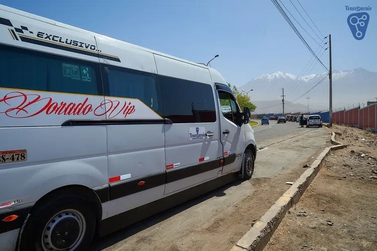 Minibús blanco estacionado al borde de la carretera con montañas al fondo y cielo azul despejado.