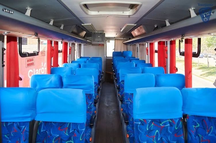 Interior de un autobús con filas de asientos de color azul brillante y un pasillo central, visto desde atrás hacia adelante.