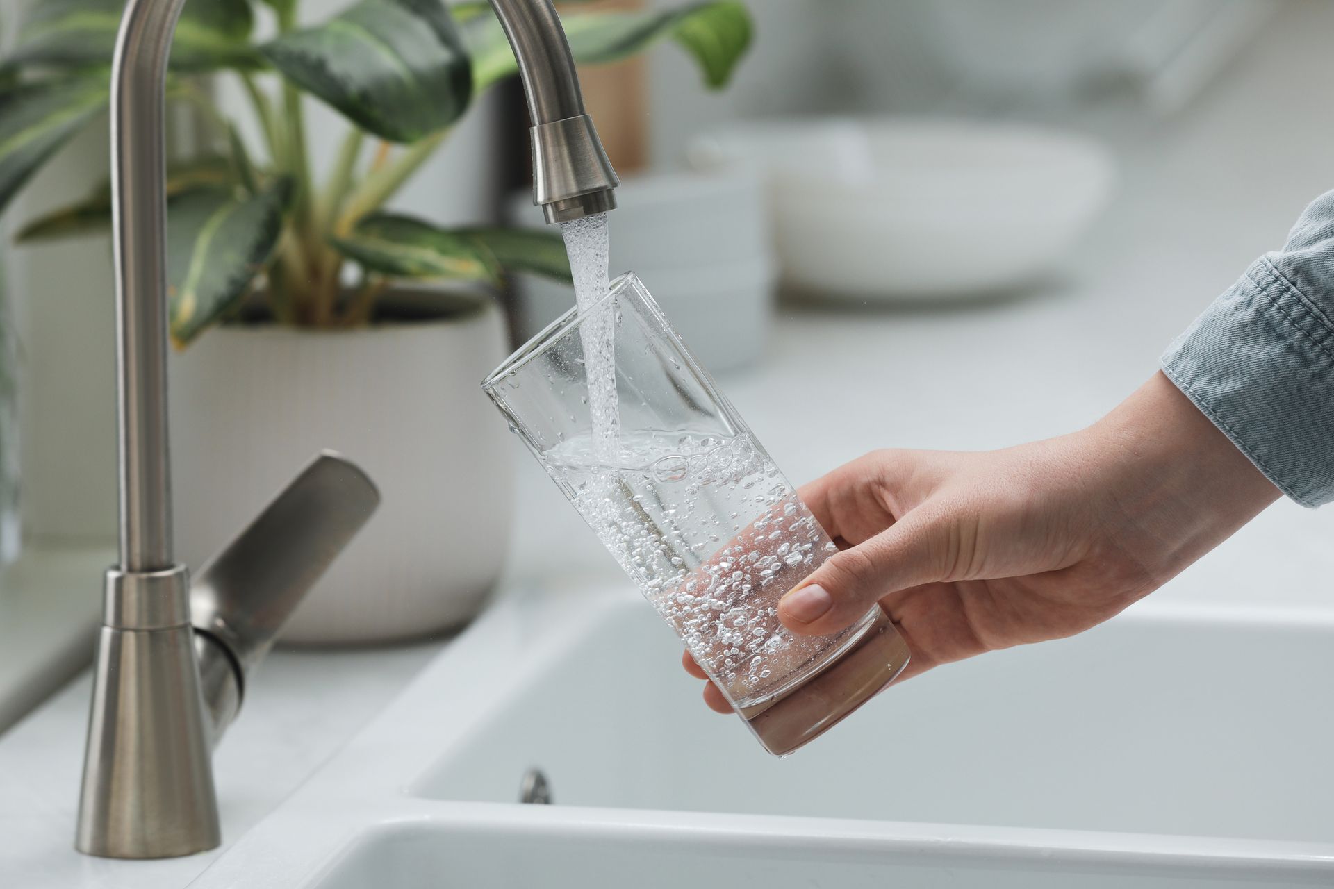 Woman filling glass with water from tap in kitchen, closeup.