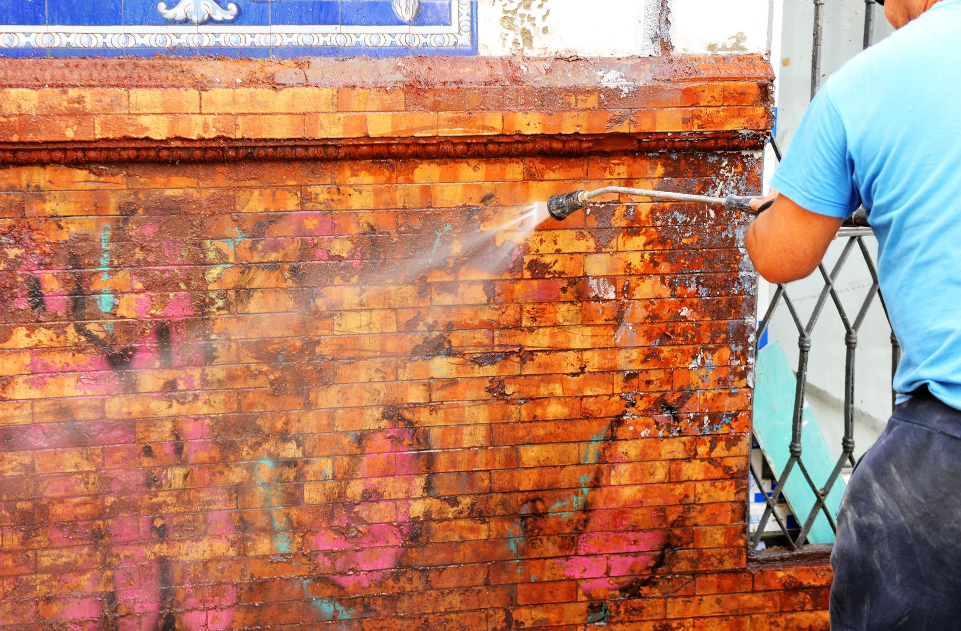 A man is cleaning a brick wall with a high pressure washer.