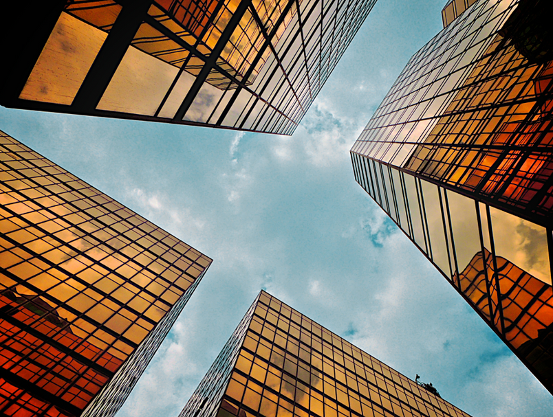 Skyscrapers with golden-toned glass reflect the sky, forming a square frame around a view of clouds.