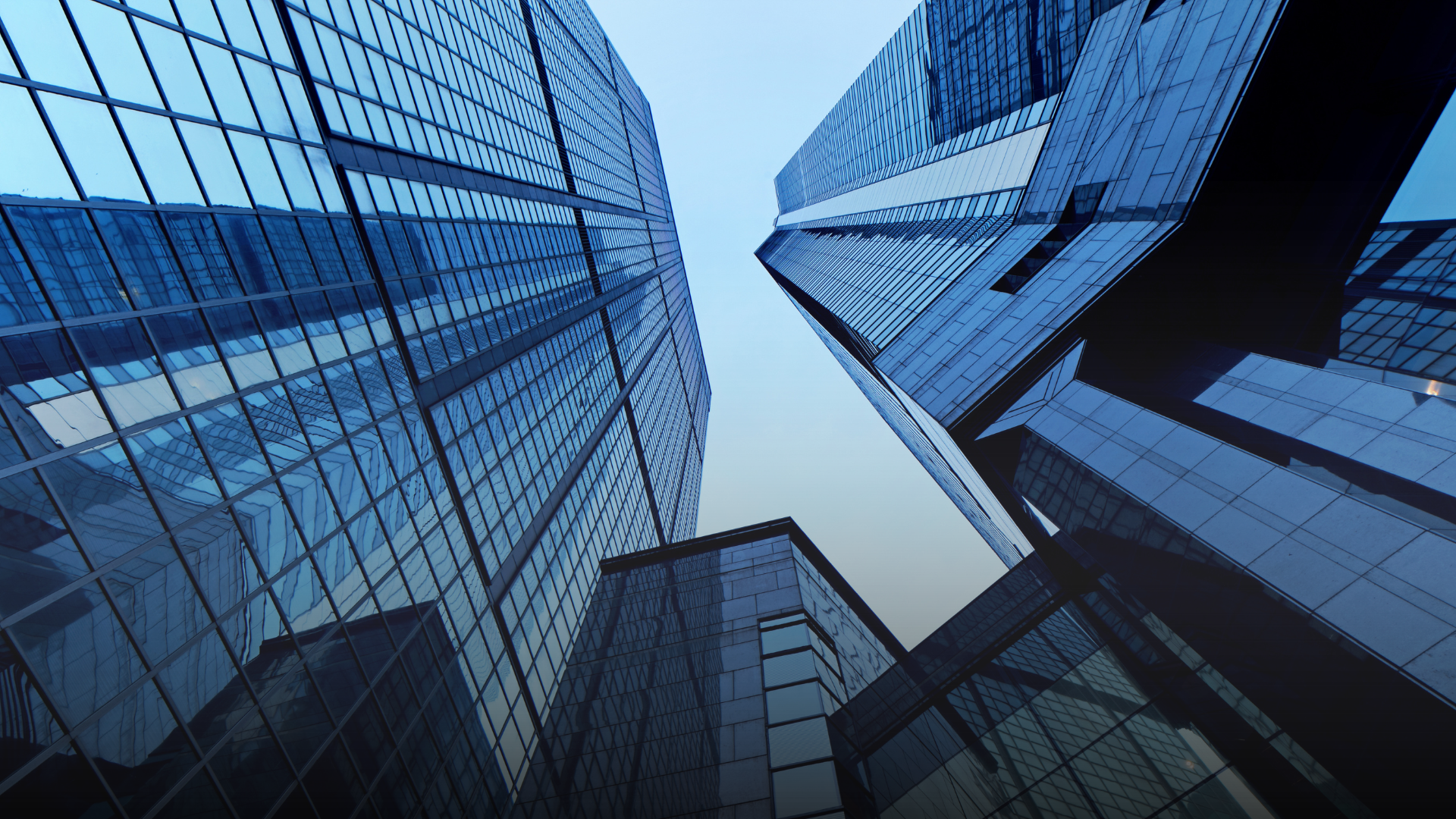 Low-angle view of modern glass skyscrapers against a blue sky.