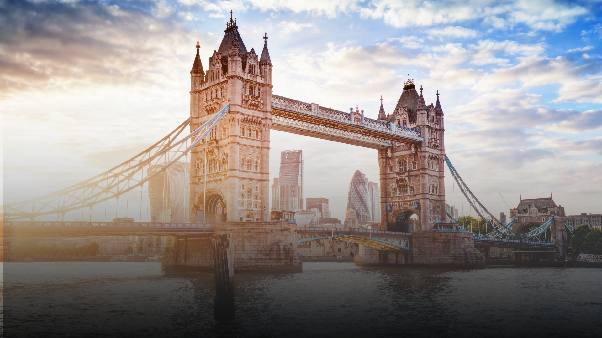 Tower Bridge in London over the Thames River at sunset; skyscrapers in the background.