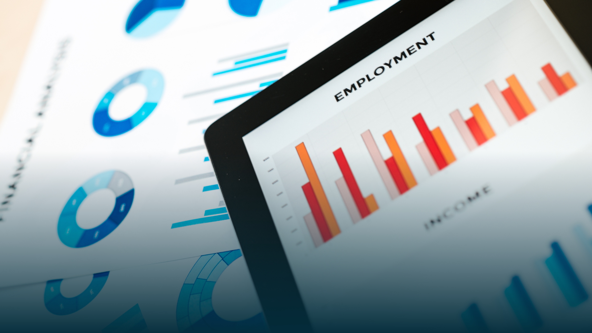 Tablet displaying employment bar graph with financial charts on paper.
